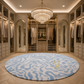 A luxury round area rug with a blue and white wavy pattern and a gold monogram, displayed in a spacious, elegantly decorated walk-in closet with a crystal chandelier.