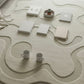Wavy beige rug with white square tiles and decorative items on a light wooden floor.
