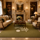 An elegant, luxurious living room featuring a large olive green area rug with a white palm leaf and circle motif in the center. The room is furnished with cream-colored sofas, matching armchairs, a dark wood coffee table, and a grand chandelier hanging from the ceiling.