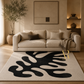 A large area rug with an abstract black organic pattern on a cream background, styled in a modern living room setting in front of a beige sofa.