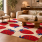 A cream-colored area rug with a bold red and blue strawberry pattern, styled in a modern living room setting with a wooden coffee table, cream sofa, and armchair.
