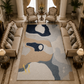 A large rectangular area rug with an abstract organic pattern in navy, beige, light blue, and cream, styled in a luxurious living room with beige sofas, armchairs, and columns.