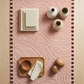 Decorative setting with wooden tray, vases, and books on a pink textured surface.