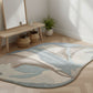 Rug with abstract design on a wooden floor in a room with a mirror and plants.