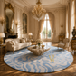 A large round area rug with a light blue and cream wavy pattern and a small gold monogram, styled in a luxurious classical living room with a beige sofa, armchair, and ornate chandelier.