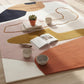 Colorful abstract rug with books, bowls, and a plant on a wooden floor.