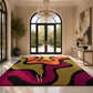 A large rectangular area rug with a bold abstract wavy pattern in olive green, magenta, orange, black, and gold, displayed in a luxurious modern entryway with a crystal chandelier and marble floors.