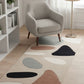 Modern living room with a gray armchair, colorful abstract rug, and white bookshelf.