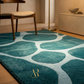Teal area rug with circular patterns in a room with wooden floor and furniture.