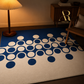 A rectangular area rug with a blue and off-white geometric pattern of overlapping circles, styled in a warm, dimly lit room next to a lamp and a wooden chair.