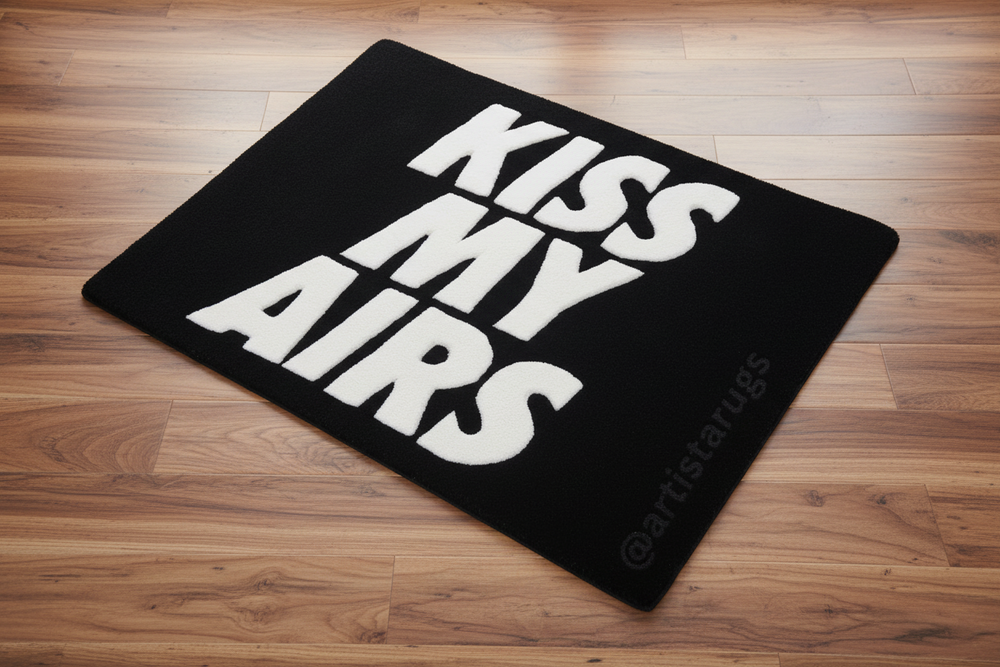Black doormat with 'KISS MY AIRS' text on a wooden floor