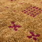 A rectangular brown area rug with a textured, heathered finish, featuring horizontal bands of small red geometric motifs and a central gold Om symbol near the bottom.