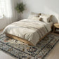Neatly made bed with beige bedding on a wooden bed frame in a room with a decorative rug.