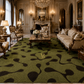 An ornate green area rug with a black abstract wavy pattern is displayed in a luxurious, vintage-style living room. The room features antique cream-colored sofas, a marble coffee table, and gold wall sconces.