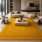 A large mustard yellow area rug with black geometric border patterns, styled in a modern living room with a curved cream sofa, two matching armchairs, and a light wood coffee table.