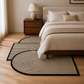 A modern bedroom scene showing a set of three semi-circular area rugs with black and beige diagonal stripes and black borders, styled on a light wood floor in front of a bed.