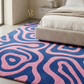 Pink and blue patterned rug in a bedroom setting with a bed and lamp.