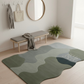 Green and gray rug on a wooden floor with a bench and mirror in the background.
