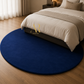 A round navy blue shag rug in a modern bedroom setting, positioned under a bed with beige bedding and a dark base.