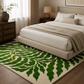 A large area rug with a bold green leaf pattern on a cream background, styled in a modern bedroom setting under a bed with neutral bedding.