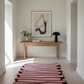Modern interior with a wooden console table, abstract art, and a pink rug.