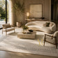 A luxury living room scene featuring a large cream-colored area rug with black dotted geometric borders, styled with a curved cream sofa, two matching armchairs, a stone coffee table, and warm ambient lighting.