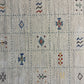 Close-up of a textured area rug with a cream-colored base, featuring a central rust-brown abstract symbol and scattered blue and gray motifs.