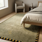 Bedroom with a green rug featuring a logo, bed, chair, and side table.