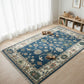 Decorative blue rug with intricate patterns on a wooden floor in a room with white curtains and shelves.