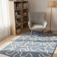Gray armchair on a blue patterned rug in a room with a bookshelf and lamp.
