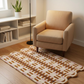 Beige armchair in a room with a patterned rug and bookshelf.