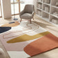 Colorful abstract rug on a wooden floor with a chair and bookshelf in the background.