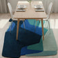 Dining table with chairs on a colorful geometric rug in a room with light-colored walls and floor.