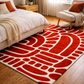 Red and white abstract patterned rug in a bedroom setting with a bed and chair.