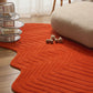 Orange textured rug on a wooden floor with a glass side table and white cushion.