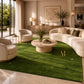A large green area rug with a subtle grass texture and small gold monogram details, styled in a luxurious modern living room with cream-colored curved sofas and a round stone coffee table.