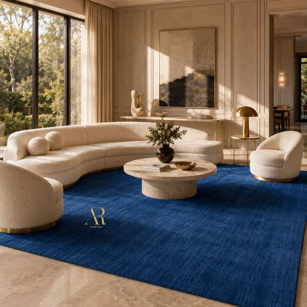 A rectangular royal blue textured rug with a small gold embroidered monogram logo in the upper right quadrant, shown flat against a plain white background.