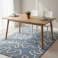 Dining table with chairs on a blue patterned rug in a room with white walls and curtains.