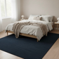 Bedroom with a bed on a dark blue rug, wooden floor, and light-colored walls.
