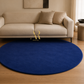 A round navy blue shag rug on a light wood floor in front of a beige fabric sofa with two matching pillows. A gold 'Artist Hugo' logo is centered below the sofa.