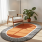 Round orange rug with black and white striped border in a room with a chair and plant.