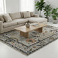 Beige sectional sofa in a living room with a patterned rug, wooden coffee table, and potted plants.