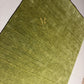 An olive green textured area rug with a small gold monogram logo in the lower right corner, displayed flat against a white background.