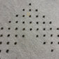 A close-up of a light gray textured fabric or carpet with a repeating pattern of small dark brown star-like motifs arranged in rows.