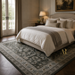 Neatly made bed in a stylish bedroom with a large rug and decorative elements.