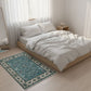 Bedroom with a bed, white bedding, and a blue patterned rug on a light wooden floor.