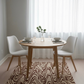 Dining room with a round wooden table and white chairs on a patterned rug.