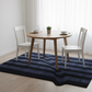 Dining table with chairs on a blue striped rug in a room with white walls and large windows.