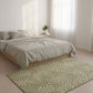 Bedroom with a bed and a green patterned rug on a light wooden floor.