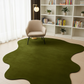 Green rug on a light wood floor with a beige armchair and white bookshelf in the background.